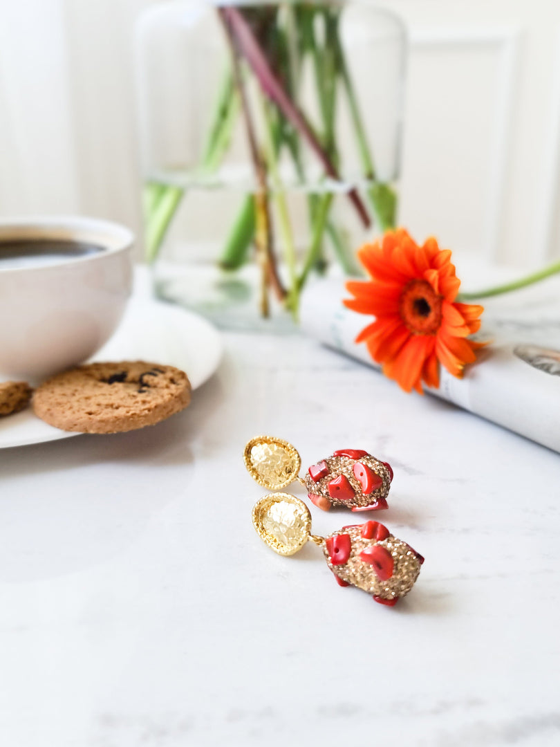 Red natural coral earrings with 24k gold plating displayed on a table near a coffee cup and bright orange flower.