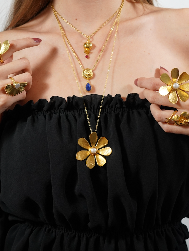 Gold flower necklace with matching rings, layered with two other necklaces.