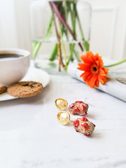 Red natural coral earrings with 24k gold plating displayed on a table near a coffee cup and bright orange flower.